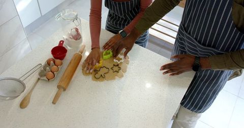 Couple cutting cookie shapes on quartz countertop wearing striped aprons for holiday baking