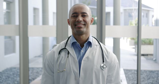 Confident biracial doctor stands in a modern hospital. His smile conveys trust and professionalism in a healthcare setting.