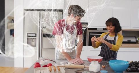 Couple baking together kneading dough and cracking eggs with flour cloud in kitchen