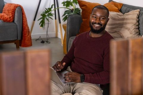 African american man working remotely on laptop in cozy midcentury living room