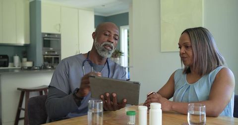 African-american nurse consulting mature woman at home using tablet to review medication