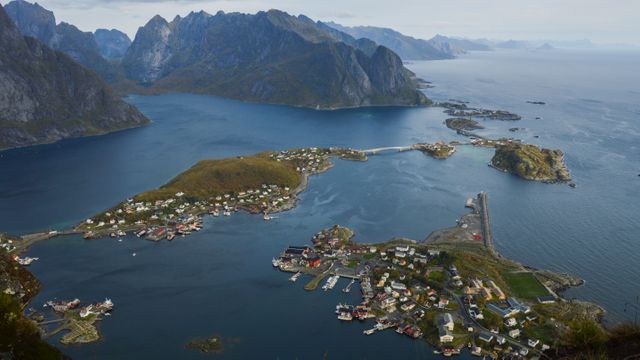 Beautiful aerial view of a quaint coastal village surrounded by majestic fjords and mountains in Norway. This scenic landscape captures the charm of small town living juxtaposed against the rugged natural beauty typical of Norwegian geography. Perfect for travel blogs, tourism advertising, and promotional materials for nature and adventure tourism.