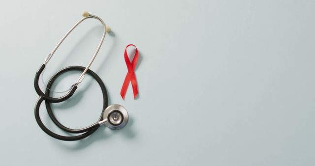 Red AIDS awareness ribbon next to a stethoscope on light blue background. Suitable for campaigns promoting AIDS awareness, healthcare programs, medical education, prevention efforts, and health support initiatives.