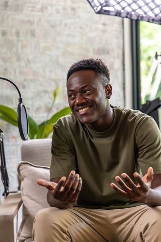 African man podcasting in home studio smiling, gesturing, engaging with audience