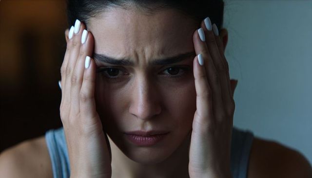 Young woman pressing temples, experiencing anxiety and tension in dimly lit portrait