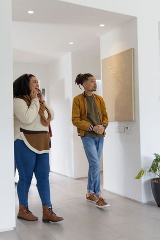 African american couple viewing textured canvas in bright modern hallway, minimalist decor