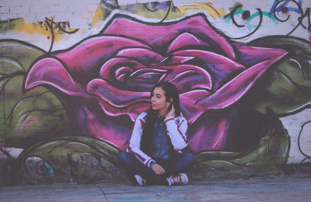 Young Woman Sitting Against Vibrant Rose Graffiti - Download Free Stock Photos Pikwizard.com
