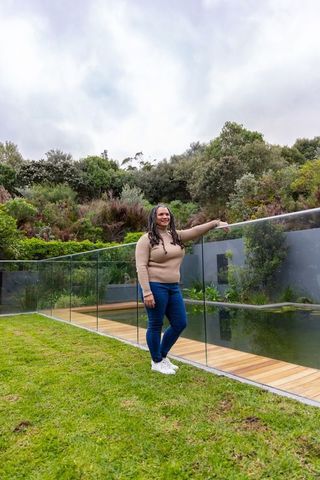 African american homeowner leaning on glass fence by backyard pond, contemporary landscape