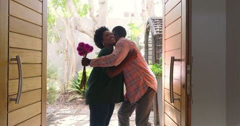 African American Couple Embracing with Flowers at Doorway