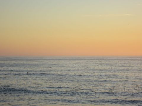 Solo paddleboarder gliding over calm ocean under pastel sunset horizon