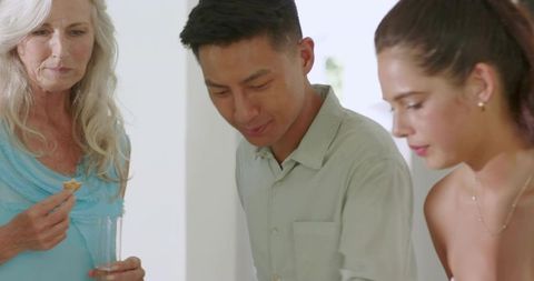 Multigenerational group leaning over table sharing snack in bright minimalist kitchen