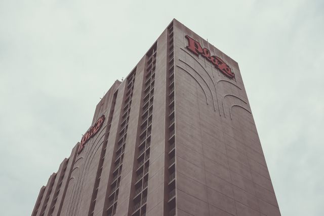Shows low angle view of a high-rise hotel building with a distinct sign against cloudy sky, highlighting modern architecture. Suitable for use in travel brochures, urban landscape collections, hotel advertisements, and architectural studies.