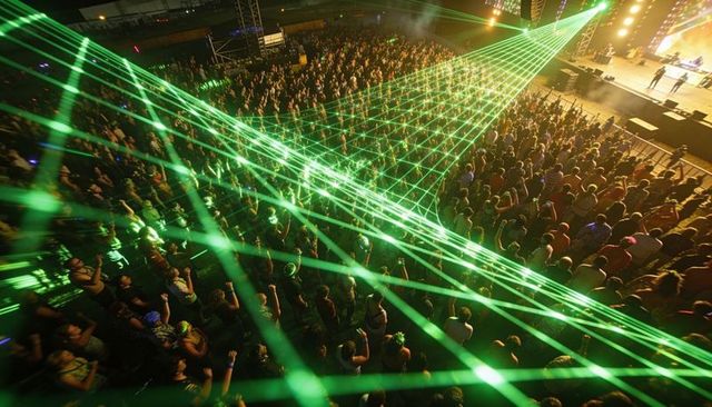Aerial view of packed festival crowd with green laser grid cutting through night sky vibes