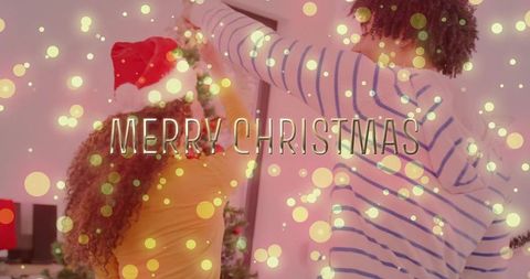 Couple decorating christmas tree at home wearing santa hat warm bokeh lights merry christmas overlay