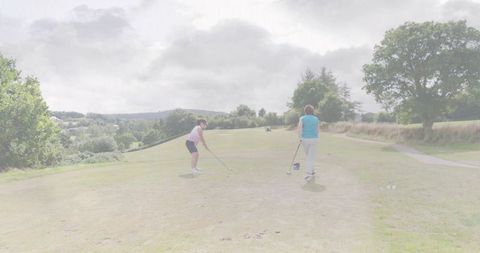 Women golfers preparing tee shot on rolling fairway under overcast sky