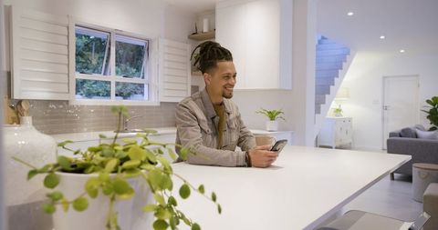 Smiling man sitting at kitchen island holding smartphone in modern open-plan home