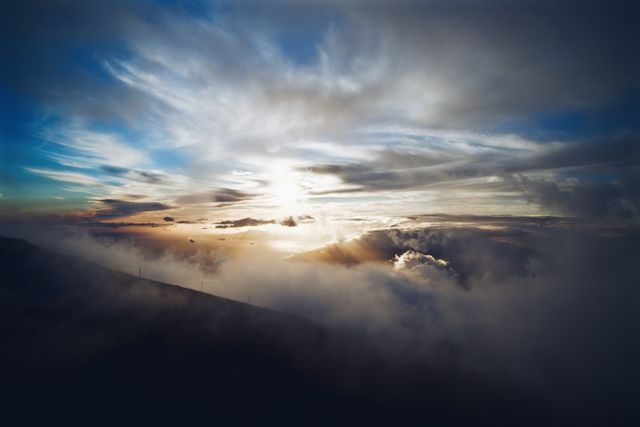 Nature scene depicting a sunrise over cloud-covered mountains. The light radiates through scattered clouds, creating a tranquil ambiance perfect for themes encompassing peace, relaxation, inspiration, and natural beauty. Useful for websites, blogs, travel promotions, posters, presentations, and scenic backgrounds.