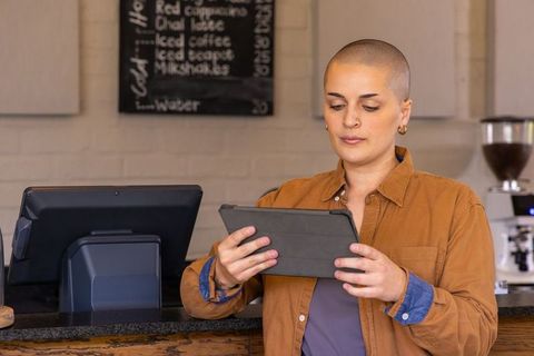 Barista checking tablet orders behind counter in rustic cafe with espresso machine