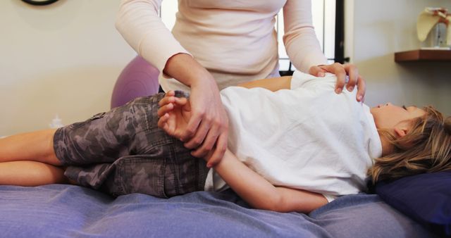 Chiropractor performing gentle therapy on young child lying on bed, focusing on back and shoulder adjustment. Useful for illustrating pediatric chiropractic care, healthcare services for children, holistic treatment methods, physical therapy for kids, wellness and recovery concepts.