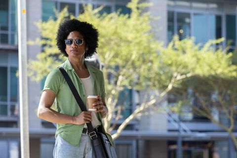 African man commuting with coffee and messenger bag, sunglasses, urban morning lifestyle