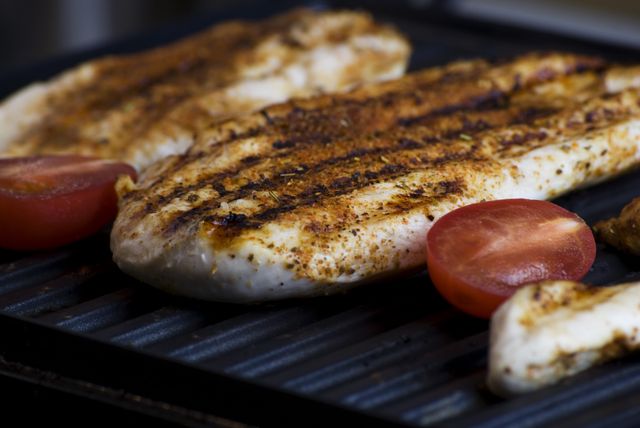 Grilled chicken breast with spices and tomato halves, perfect for illustrating healthy eating, cooking techniques, diets, and protein-rich meals. Great for culinary blogs, dietary websites, and fitness-related content.