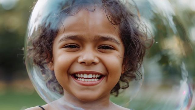 Smiling child inside giant soap bubble outdoors with curly hair and bright sunlight