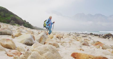 Senior Woman Trekking Beach Amid Scenic Mountain Backdrop