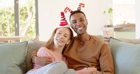Couple embracing on sofa wearing festive candy cane headbands