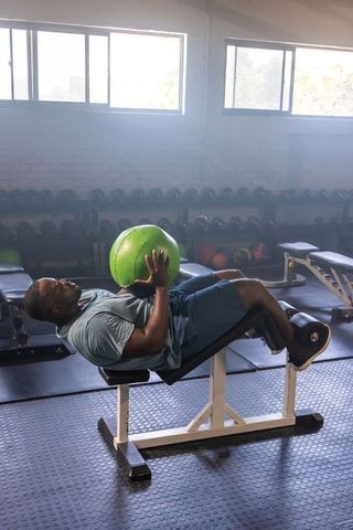 African man doing decline bench medicine ball crunch holding bright green fitness ball