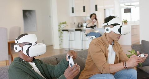 Friends Wearing White VR Headsets Playing Multiplayer Game on Modern Living Room Sofa