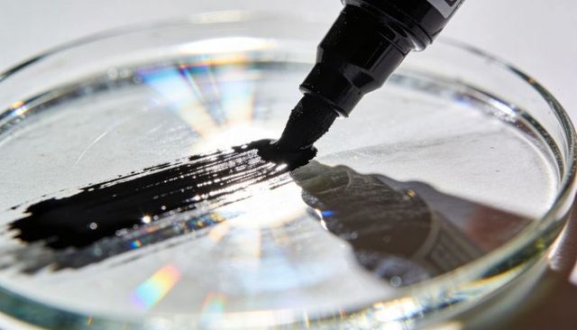 Macro black marker tip dragging ink across glass petri dish with rainbow diffraction