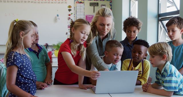 Teacher assisting a group of elementary school students with a computer during a lesson. This can be used to depict learning environments, teamwork, educational technology usage, and classroom settings. Ideal for education materials, school websites, and articles about primary education or teaching methods.