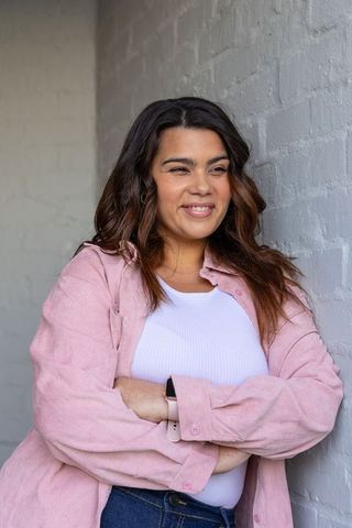 Smiling woman leaning against painted brick wall wearing pink overshirt and smartwatch