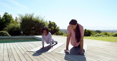 Mother and daughter practicing plank pose outdoors on wooden deck