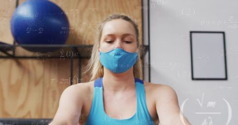 Young woman rowing in gym wearing blue mask and athletic tank, focused indoor workout