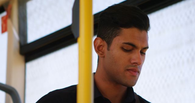 This image shows a young man traveling on public transportation, giving a glimpse into urban life and daily commute. It can be used in articles or advertisements related to city commuting, public transport services, lifestyle blogs, or campaigns promoting the use of public transportation. The thoughtful expression of the man adds a human element, making it suitable for content focused on personal stories or urban experiences.