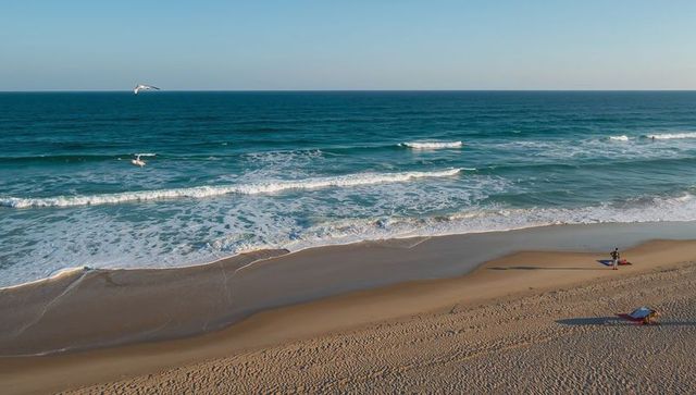 Aerial coastal sunrise showing gentle waves, sandy shoreline and two people on beach