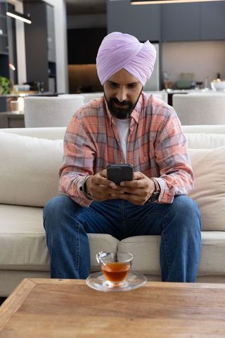 Indian man wearing lavender turban using smartphone in cozy home