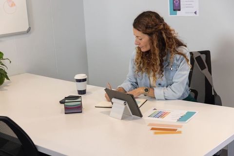 Mature designer woman working with tablet and color swatches in small meeting room