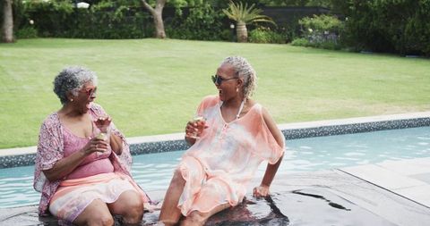 Senior friends enjoying relaxation by pool with refreshing drinks in summer
