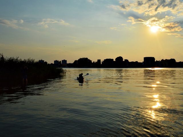 Serene sunset with silhouettes of kayaker and urban landscape. Ideal for conveying calm and peaceful vibes, urban recreation, and outdoor activities use.
