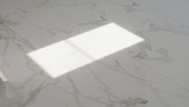Rectangular sunlight patch casting over polished carrara marble tile floor with grout lines