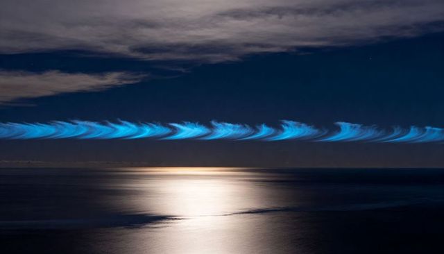 Cyan ribbon of light stretching over moonlit ocean nightscape, surreal long exposure