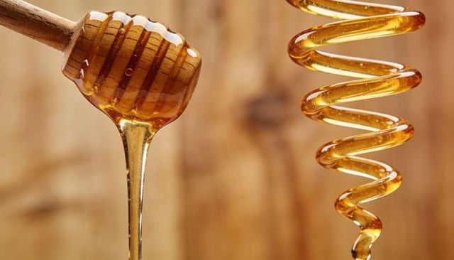 Dripping honey dipper releasing thick amber stream with glossy viscous spiral honey coil