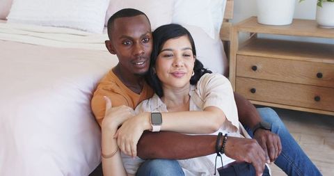 Multiracial couple cuddling on bedroom floor with smartwatch health icons conveying calm