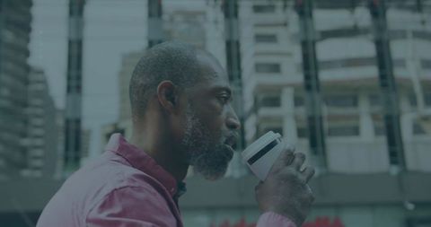 Contemplative mature man drinking coffee from travel cup on urban plaza with glass facades