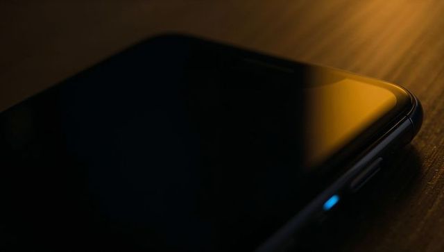 Resting smartphone on wooden tabletop reflecting warm amber light with blue led, rim glow