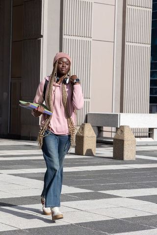 African american teen walking campus in pink hoodie carrying notebooks and backpack