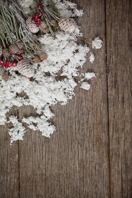 Pine cones and red berries with fake snow on a wooden plank create a rustic and festive winter scene. Ideal for holiday greeting cards, seasonal advertisements, Christmas decorations, and winter-themed designs. The natural elements and wood texture add a cozy and warm feel to any project.