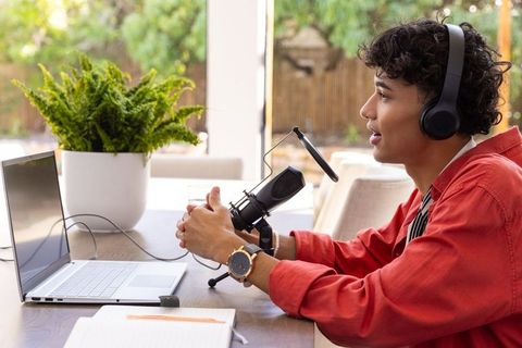 Young man recording podcast at home desk with laptop